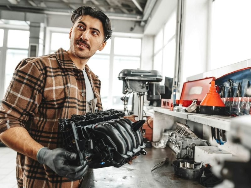 young-man-mechanic-repairing-car-parts-on-worktable-in-car-service-shop